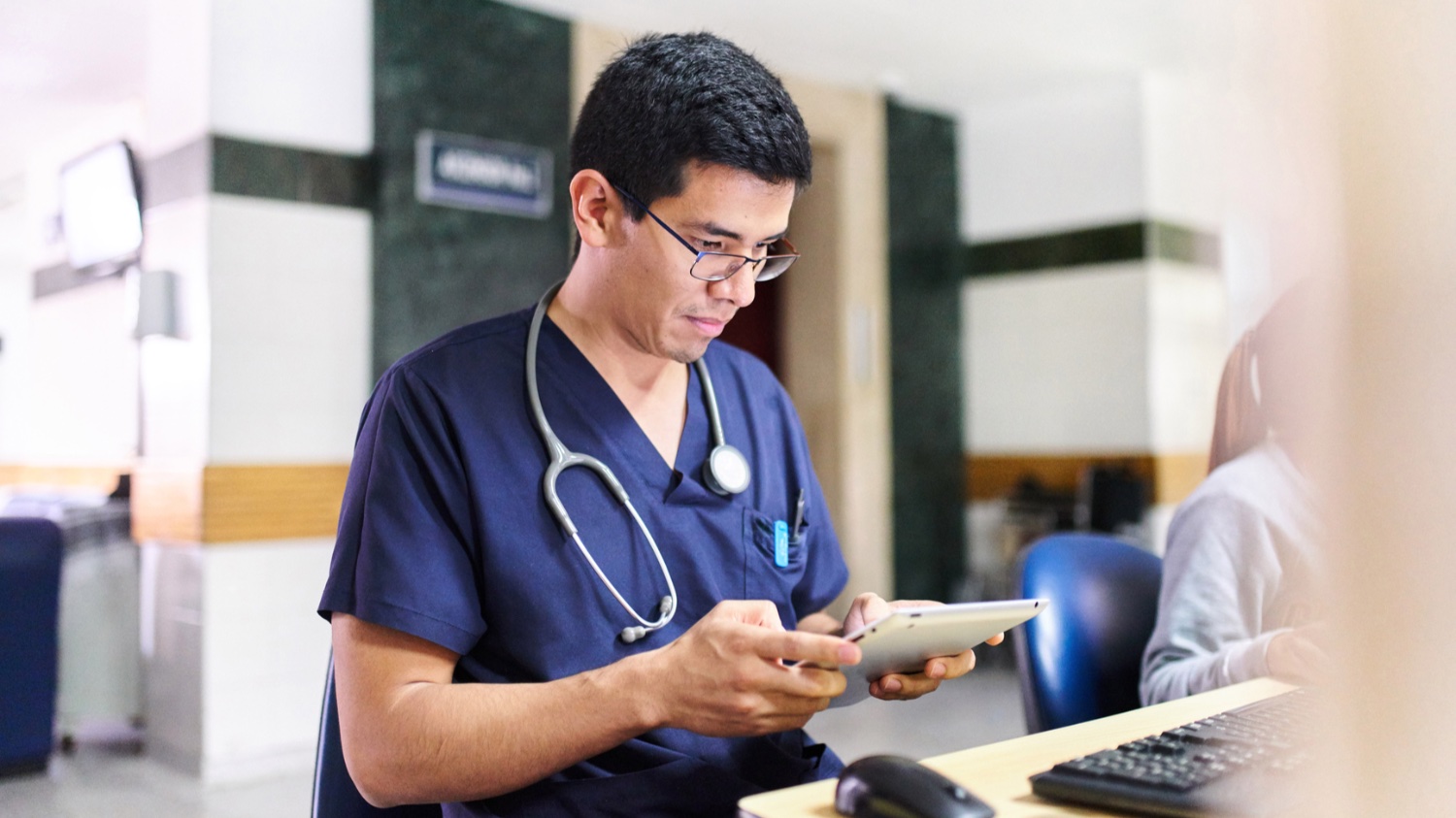 Man with stethoscope around his neck looks at a tablet.